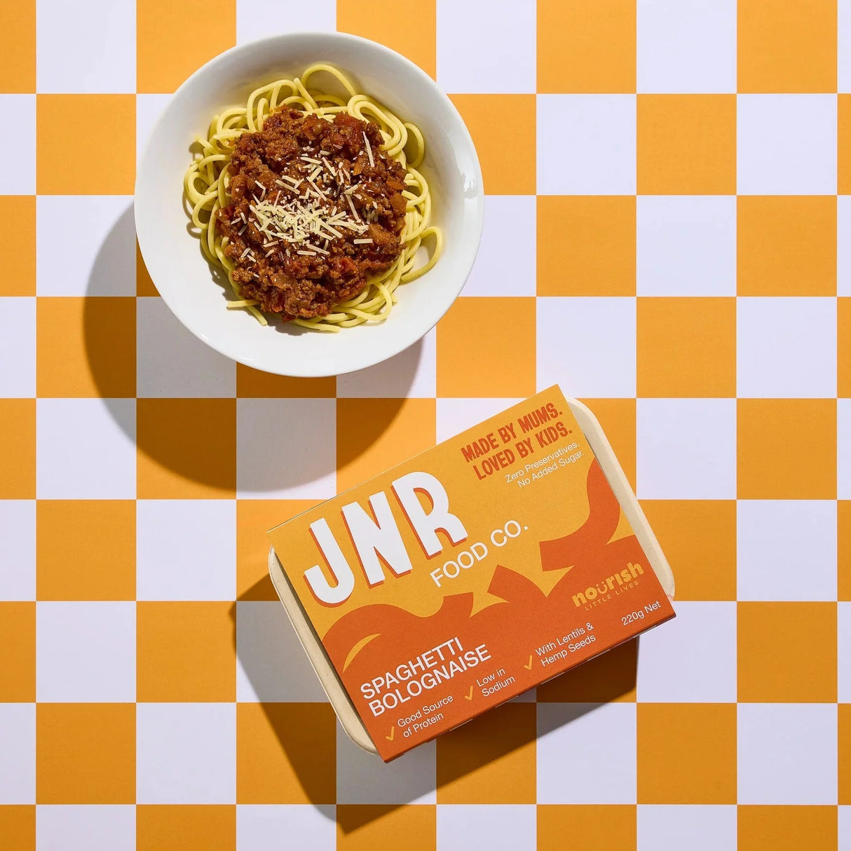 Bowl of spaghetti bolognese with JNR Food Co box on a checkered orange and white background