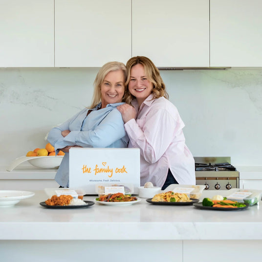 Two people standing in a kitchen with The Family Cook served meals on the counter