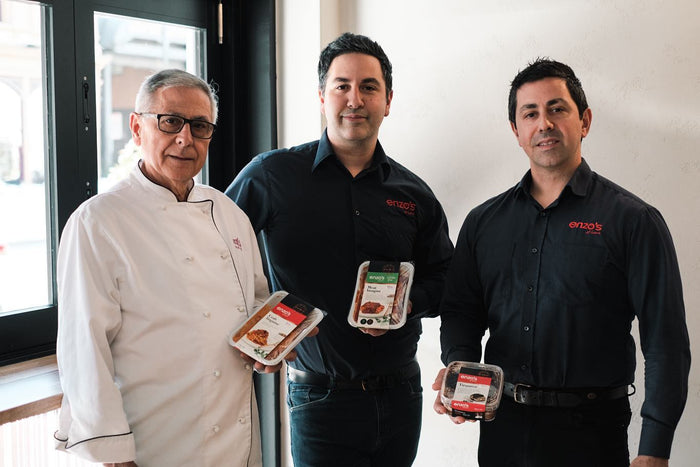 Three men holding packages of ground beef in a kitchen setting