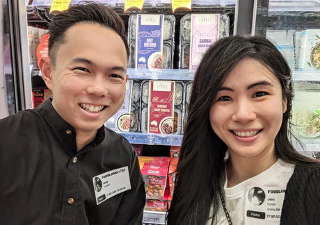Two employees standing in front of a grocery store shelf with products.