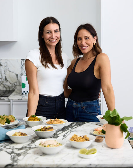 Two women standing in a kitchen with a table full of food.