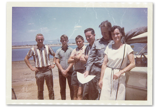 Group of people standing by a car near a body of water with a scenic background