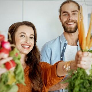 Man and woman holding a variety of fresh vegetables in a kitchen setting
