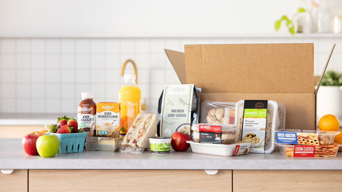 Grocery items including fruits, vegetables, and packaged goods on a kitchen counter with a cardboard box.