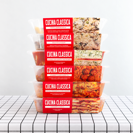 A stack of packaged meals from Cucina Classica on a table