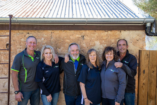 Group of six people posing in front of a rustic building.
