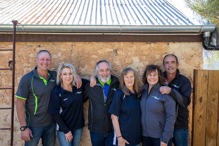 Group of six people posing in front of a rustic building.