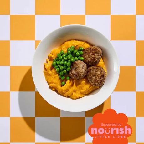 White bowl with sweet potato mash, green peas, and brown meatballs on a yellow and white checkered background with 'nourish little lives' logo.