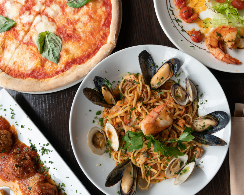 seafood pasta, pizza and meatballs on a wooden table